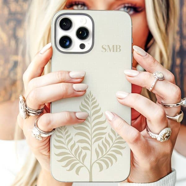 Close-Up Of A Woman'S Hands Holding A Cream-Colored Iphone Case Featuring A Beige Leaf Design And Initials.