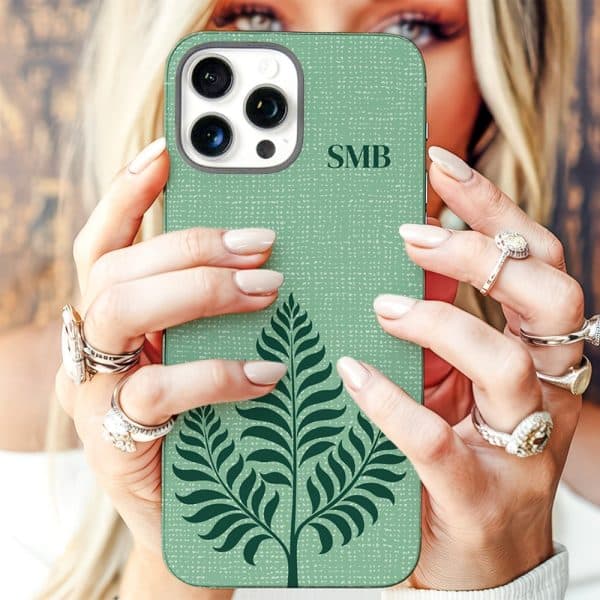 A Woman'S Hands Hold Up A Sage Green Iphone Case Featuring A Dark Green Fern Design And Personalized Initials.