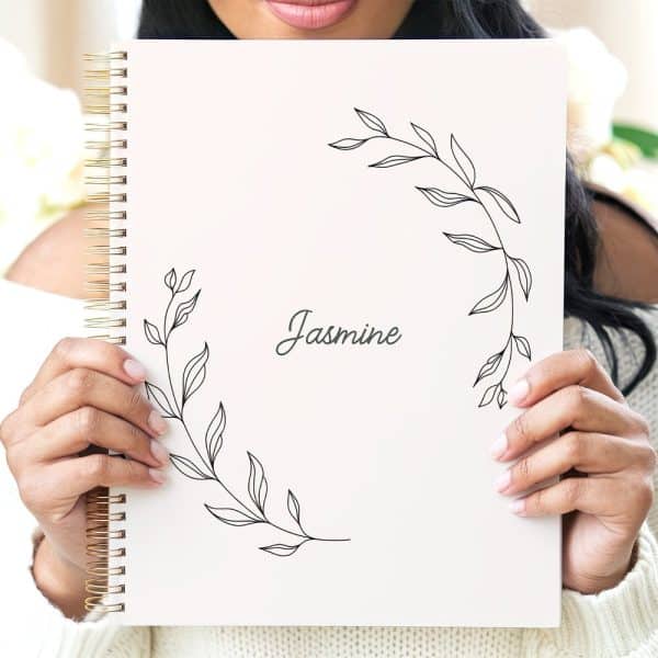 Person Holding A White Spiral Notebook With A Floral Design And The Name Jasmine.