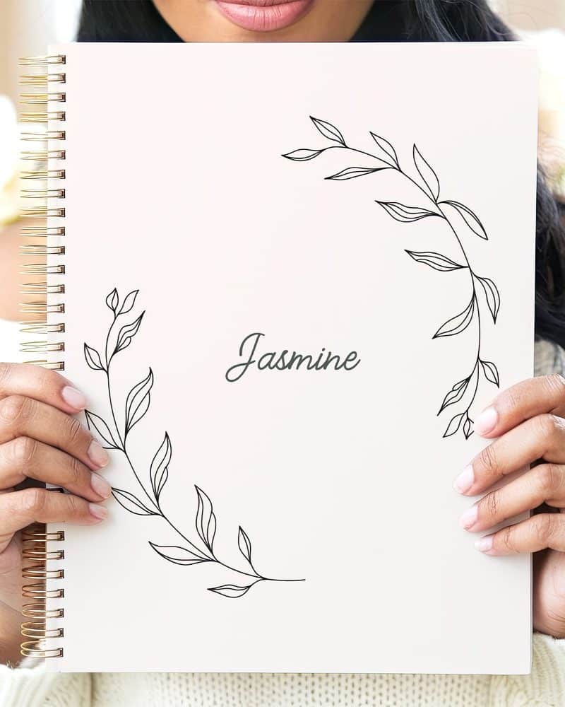Person holding a white spiral notebook with a floral design and the name Jasmine.