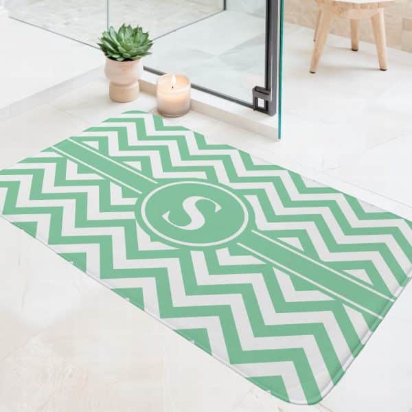 Light Green And White Chevron Patterned Bath Mat With A Central Monogram Of The Letter S.