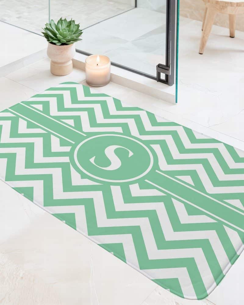 Light green and white chevron patterned bath mat with a central monogram of the letter S.