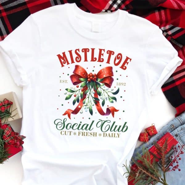 White T-Shirt With A Christmas Design Featuring A Mistletoe Sprig Tied With A Red Bow, Text Reading Mistletoe Social Club, And The Year 1892.