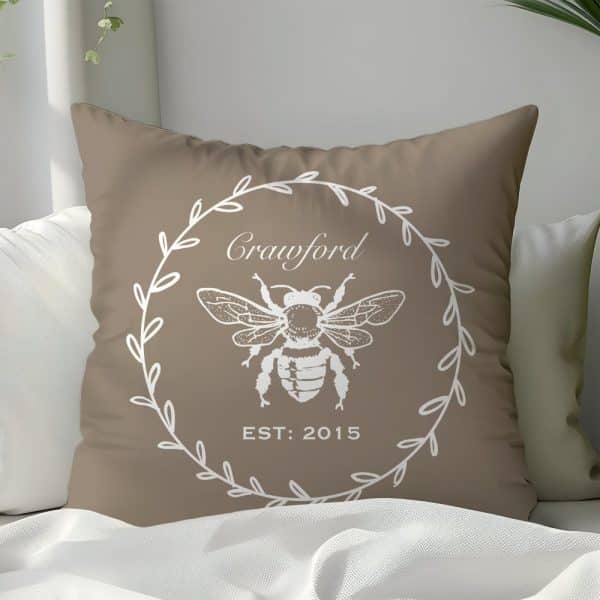 Tan Throw Pillow With A White Bee Illustration In A Wreath Design, The Name Crawford, And The Year 2015.