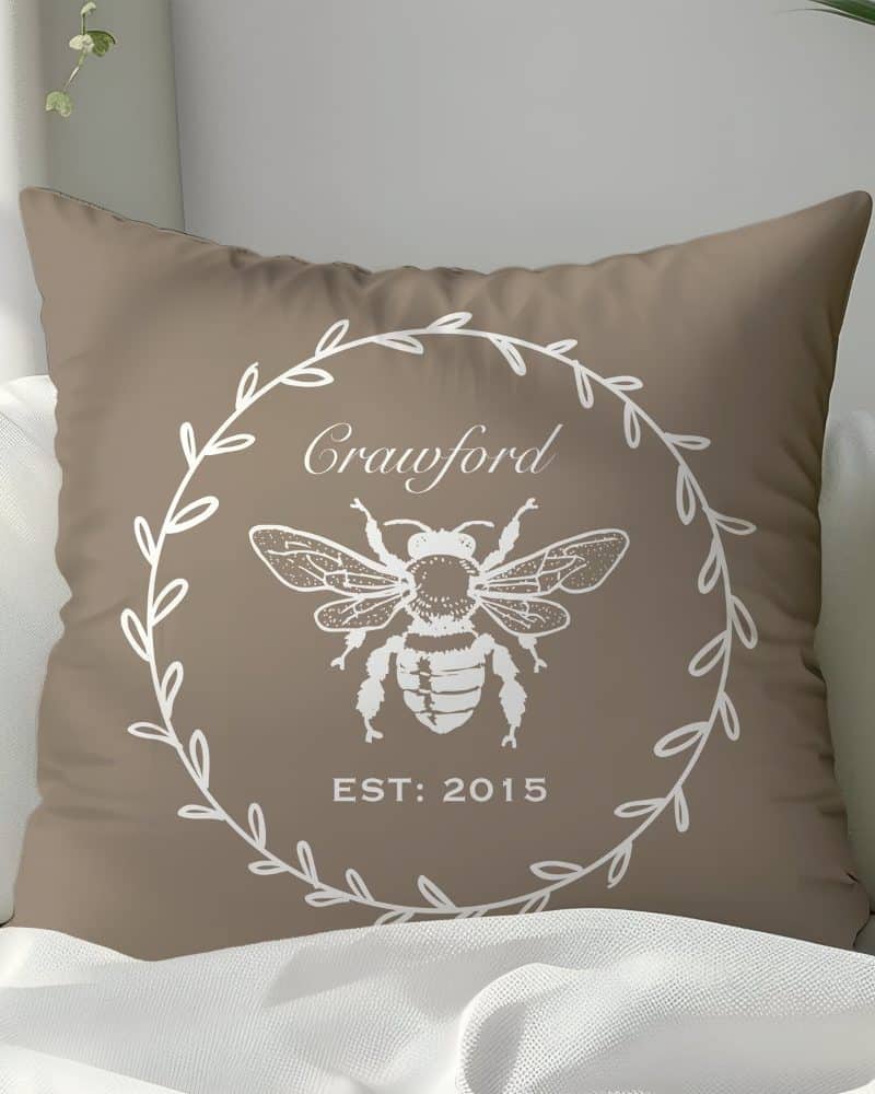 Tan throw pillow with a white bee illustration in a wreath design, the name Crawford, and the year 2015.
