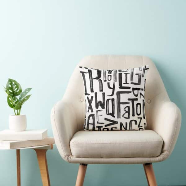 Beige Armchair With A Black And White Alphabet Pillow.