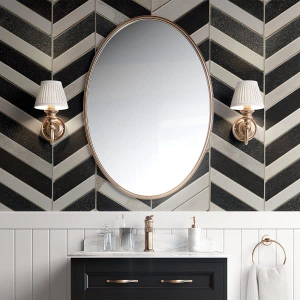 Oval Mirror Above A Dark Vanity With A Marble Countertop, Flanked By Wall-Mounted Lights, All Set Against A Black And White Herringbone Tile Wall.