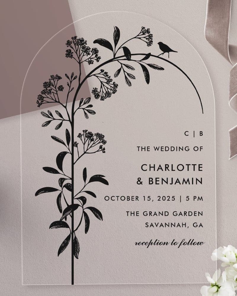 Arch-shaped clear acrylic wedding invitation with black floral illustration and wedding details.