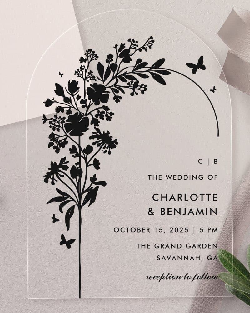Clear acrylic wedding invitation with black floral design and wedding details.