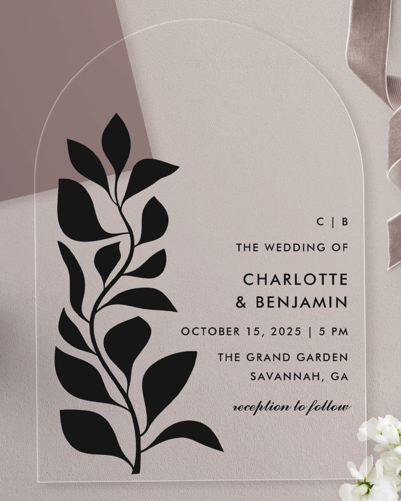 Clear acrylic wedding invitation with a black floral design and wedding details for Charlotte and Benjamin.
