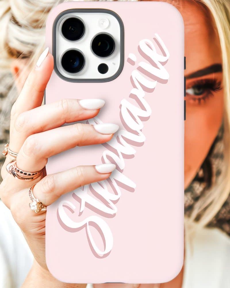 A woman's hand holds up a light pink iPhone case with the name Stephanie written in stylized white script.