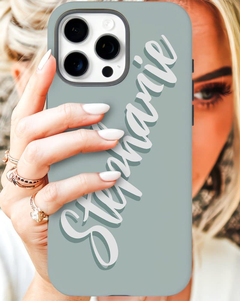 A woman's hand holds a light teal iPhone case with the name Stephanie written in stylized white lettering.