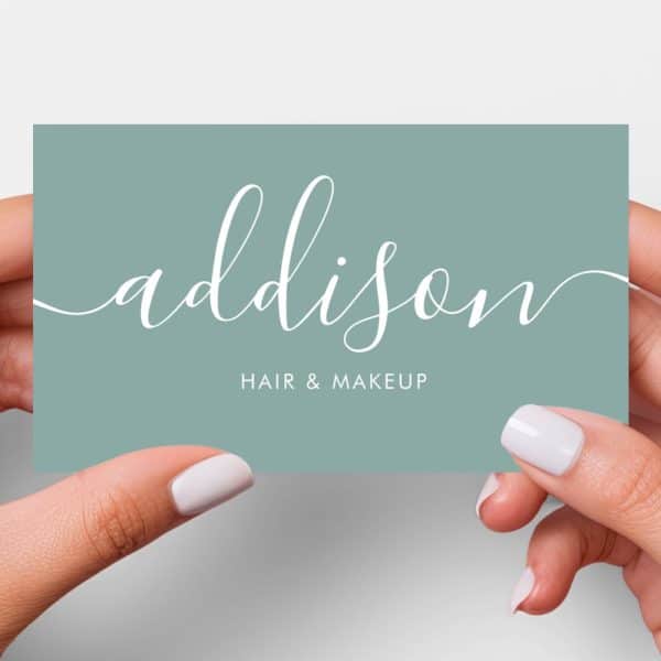 Two Hands Hold A Light Teal Business Card With The Name Addison In Elegant White Script, Followed By Hair &Amp; Makeup In Smaller White Text.