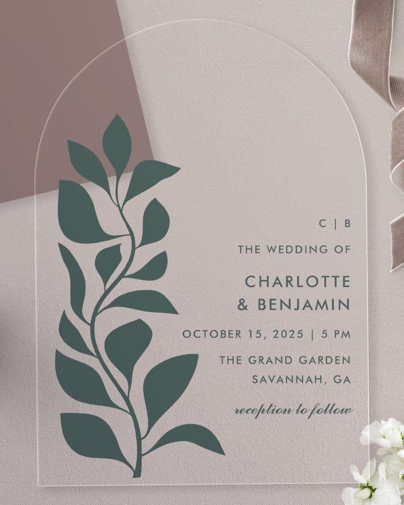 Arch-shaped clear acrylic wedding invitation with a dark green stylized floral design and the names Charlotte and Benjamin.