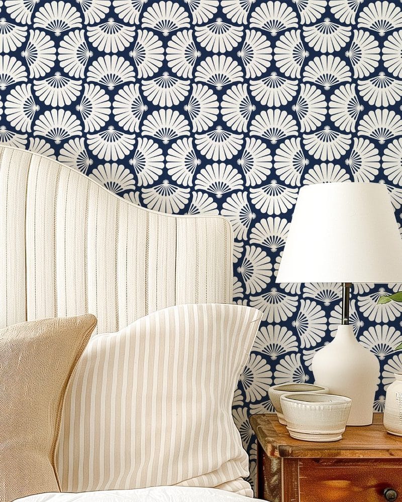 A bed with beige striped pillows against a wall covered in navy blue wallpaper featuring a repeating off-white fan pattern.