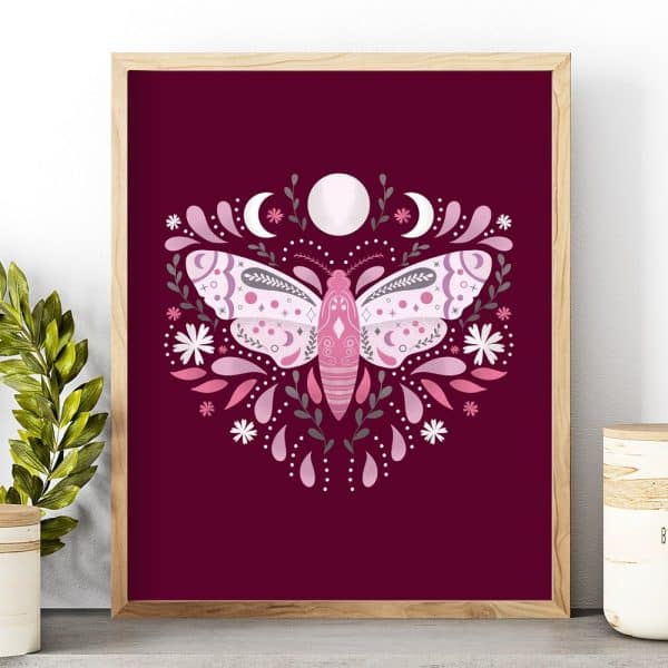 Framed Illustration Of A Pink Moth Surrounded By Flowers And Crescent Moons On A Burgundy Background.