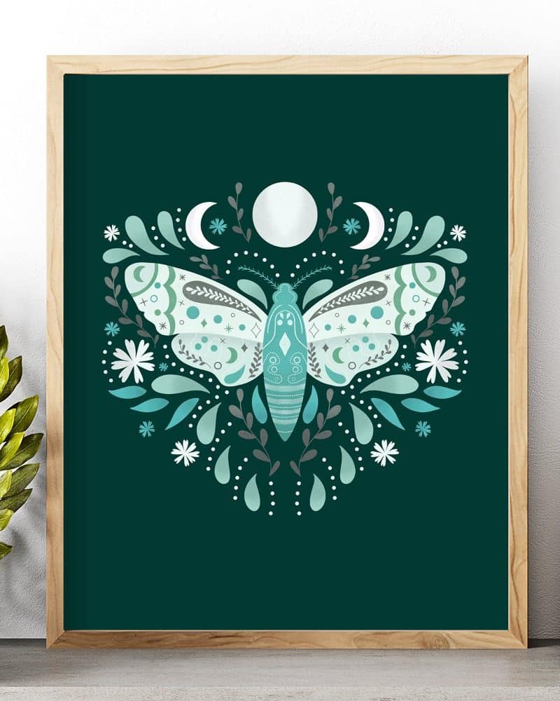 Framed artwork depicting a teal moth centered in a floral design against a dark green background.