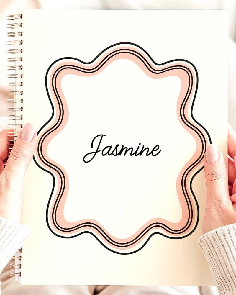 Two hands hold a spiral notebook featuring the name Jasmine within a decorative, peach-colored frame.