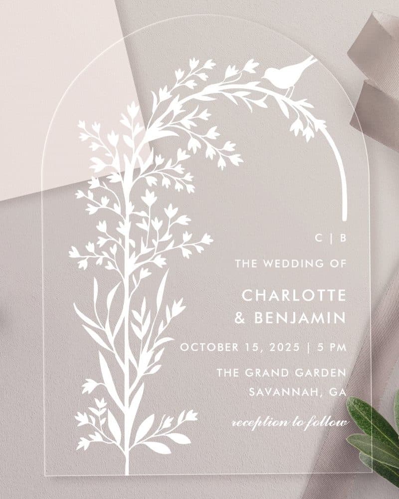 Clear acrylic wedding invitation with a floral design and bird, announcing Charlotte and Benjamin's wedding.