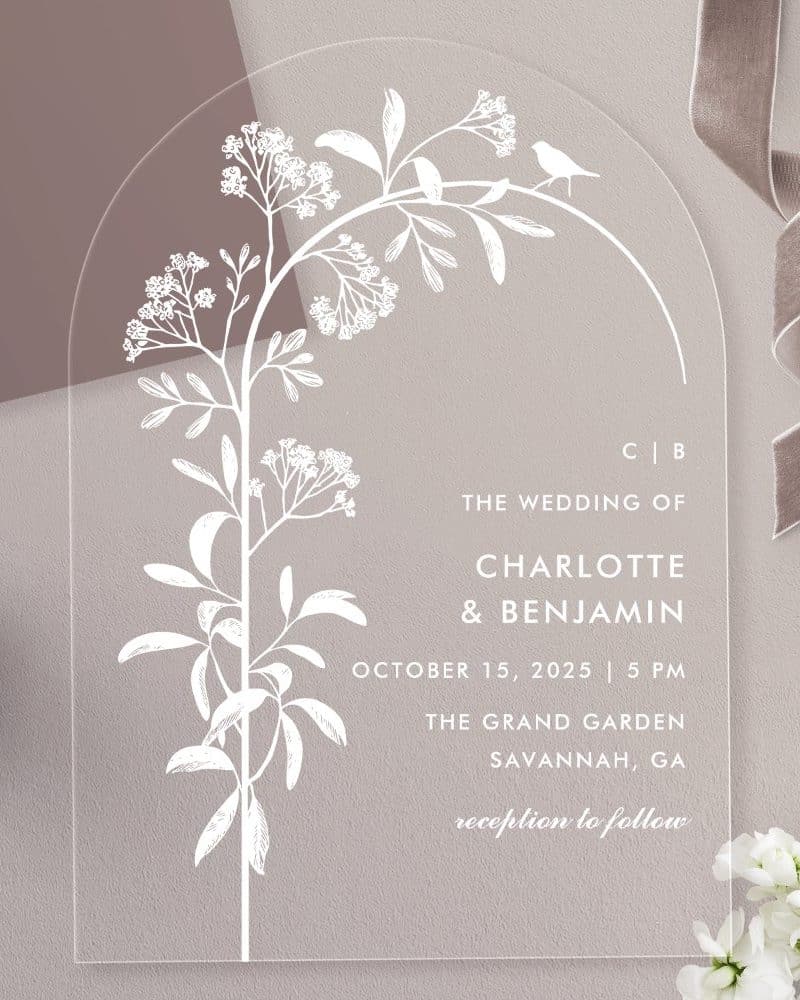 Arch-shaped clear acrylic wedding invitation with white floral illustration and wedding details.
