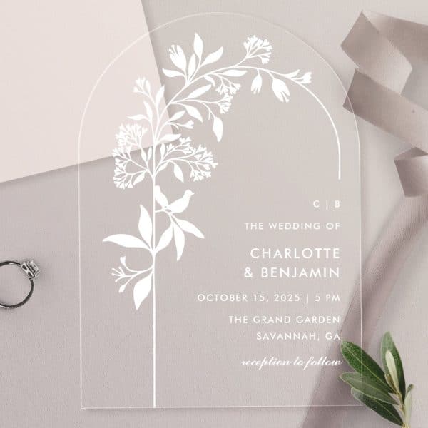 Clear Acrylic Wedding Invitation With A Floral Design And The Names Charlotte And Benjamin.