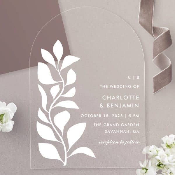 Arch-Shaped Clear Acrylic Wedding Invitation With A White Stylized Floral Design And Wedding Details.