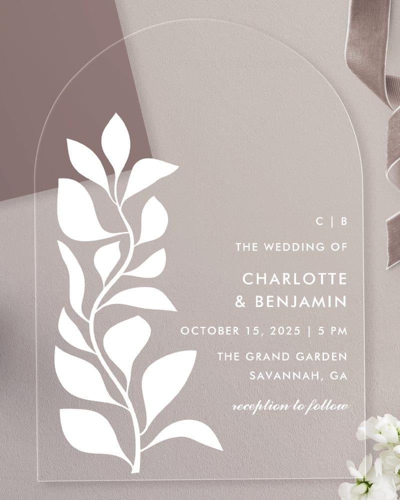 Arch-shaped clear acrylic wedding invitation with a white stylized floral design and wedding details.