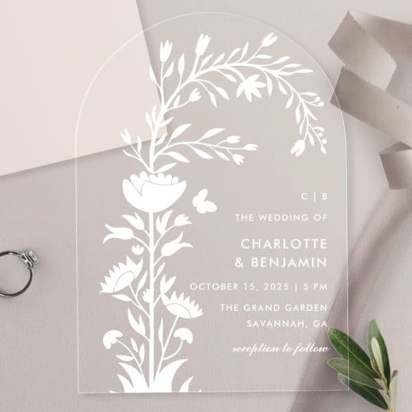 Arch-Shaped Acrylic Wedding Invitation With A Floral Design And The Names Charlotte And Benjamin.
