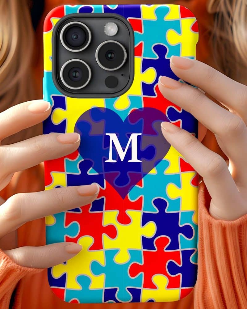 Person holding a phone case with a puzzle pattern and a heart containing the letter M.