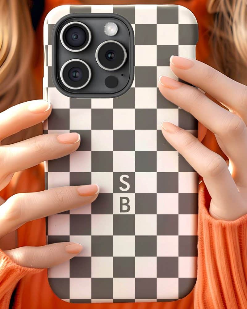 Close-up of hands holding a phone in a black and white checkered case with the initials SB.