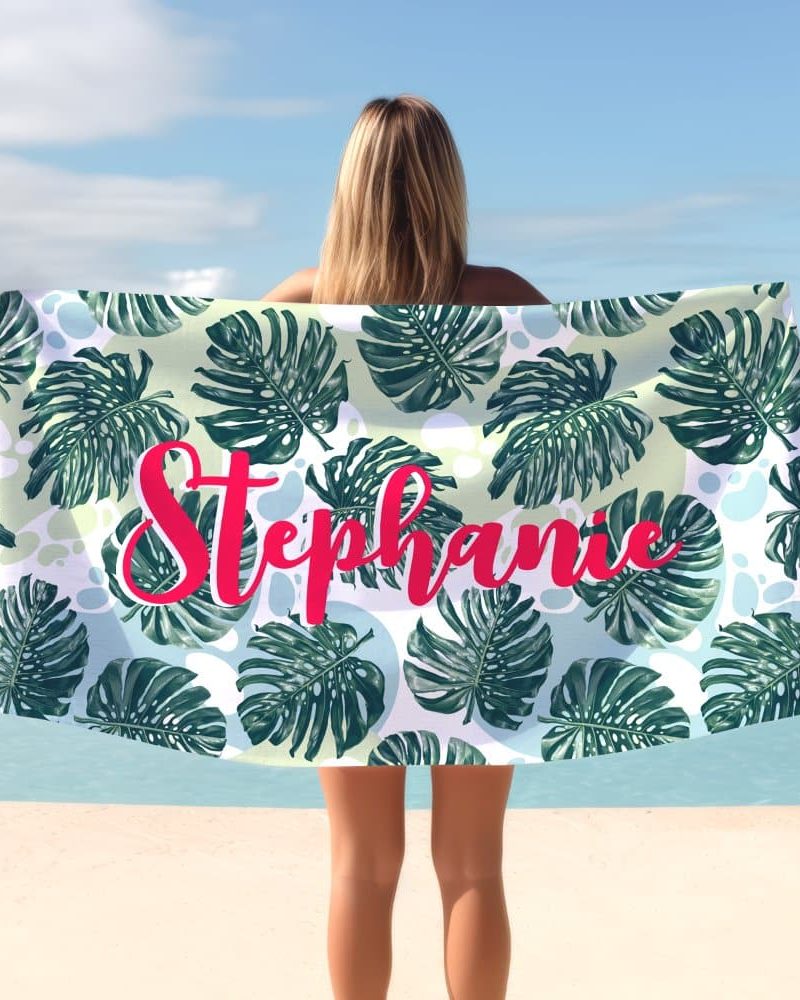 A woman holds a personalized beach towel featuring a tropical leaf pattern and the name Stephanie.