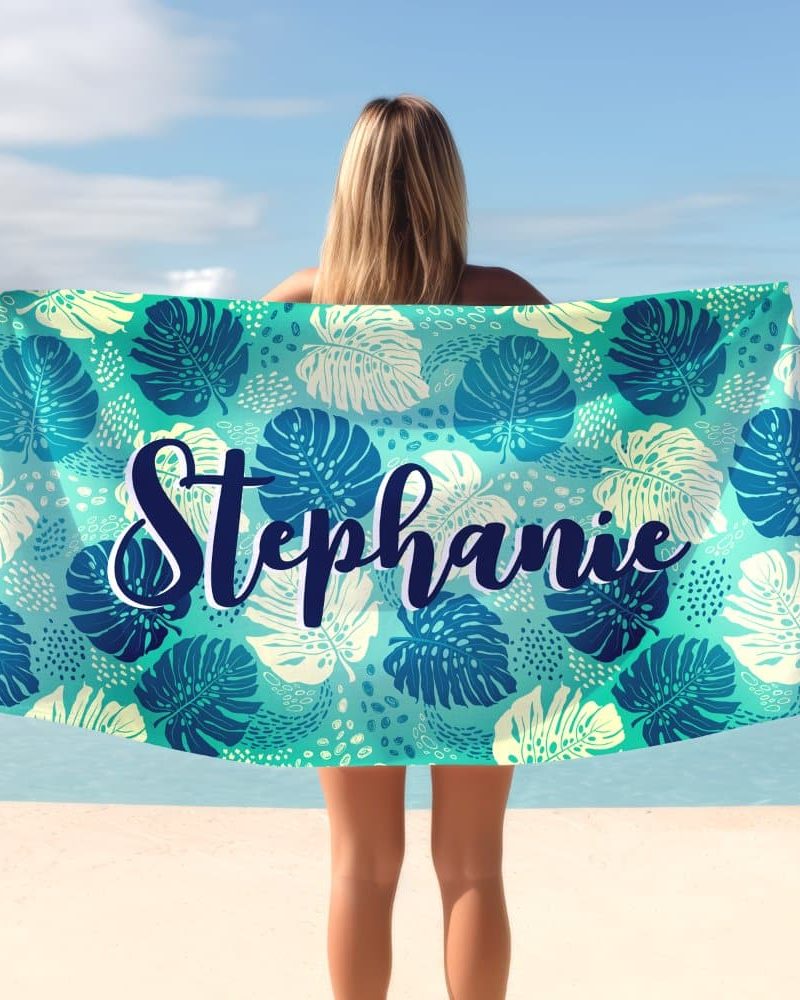 A teal beach towel with a tropical leaf pattern and the name Stephanie printed on it.