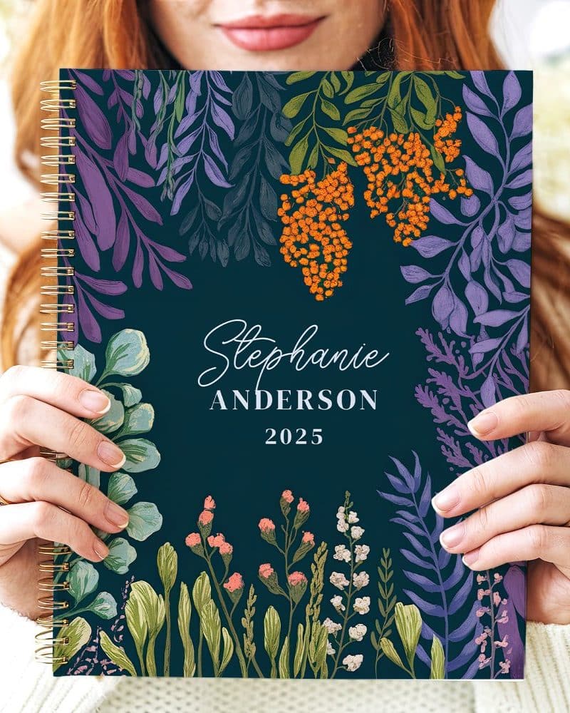 A 2025 spiral-bound planner with a dark teal cover featuring a floral design and the name Stephanie Anderson.