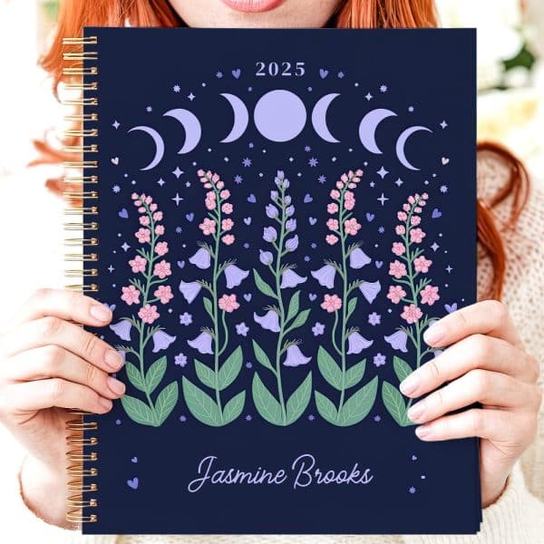 Person Holding A 2025 Spiral-Bound Planner Featuring A Dark Blue Cover With Floral And Moon Phase Illustrations. The Name Jasmine Brooks Is Printed At The Bottom.