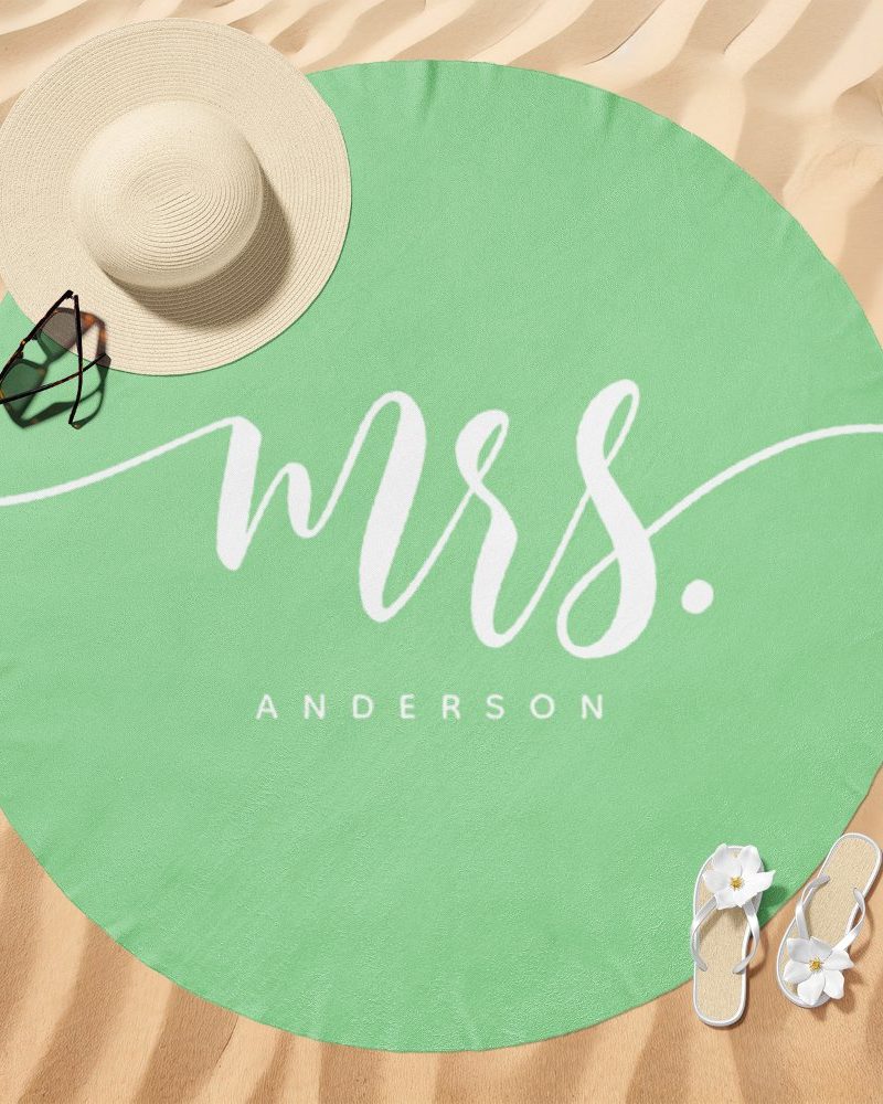 A light green round beach towel with Mrs. Anderson written in a stylized white script.