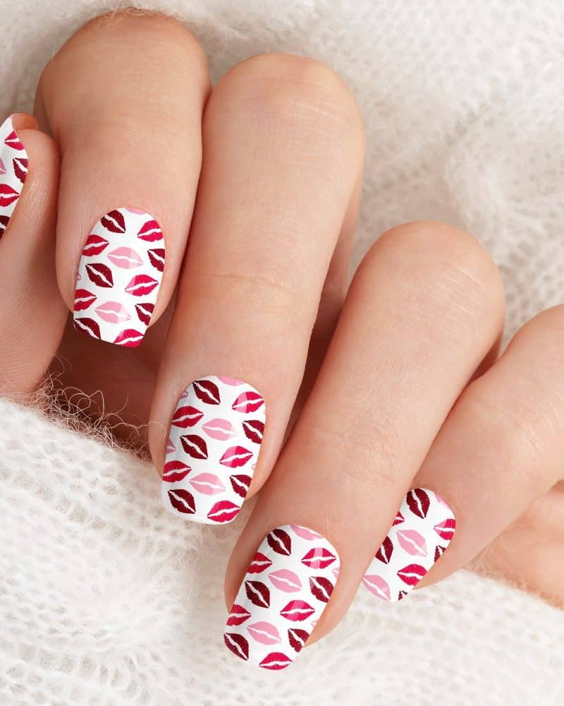 Closeup of a hand displaying fingernails with a pink and red lipstick print design.