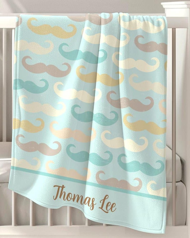 Personalized baby blanket with a light blue background and a repeating pattern of mustaches in various pastel colors. The name Thomas Lee is embroidered on the bottom.