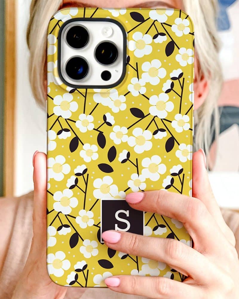 A yellow iPhone case with a white floral pattern and a black initial S.