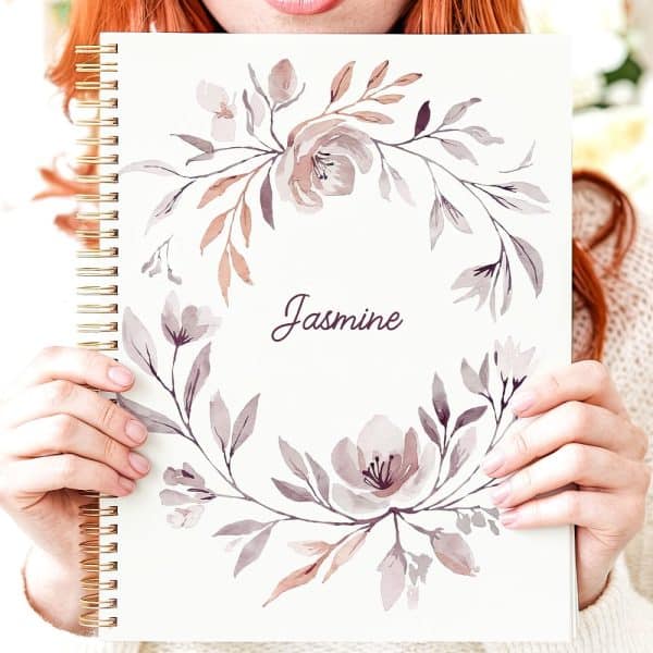 Person Holding A Spiral-Bound Notebook Featuring A Watercolor Floral Design And The Name Jasmine.