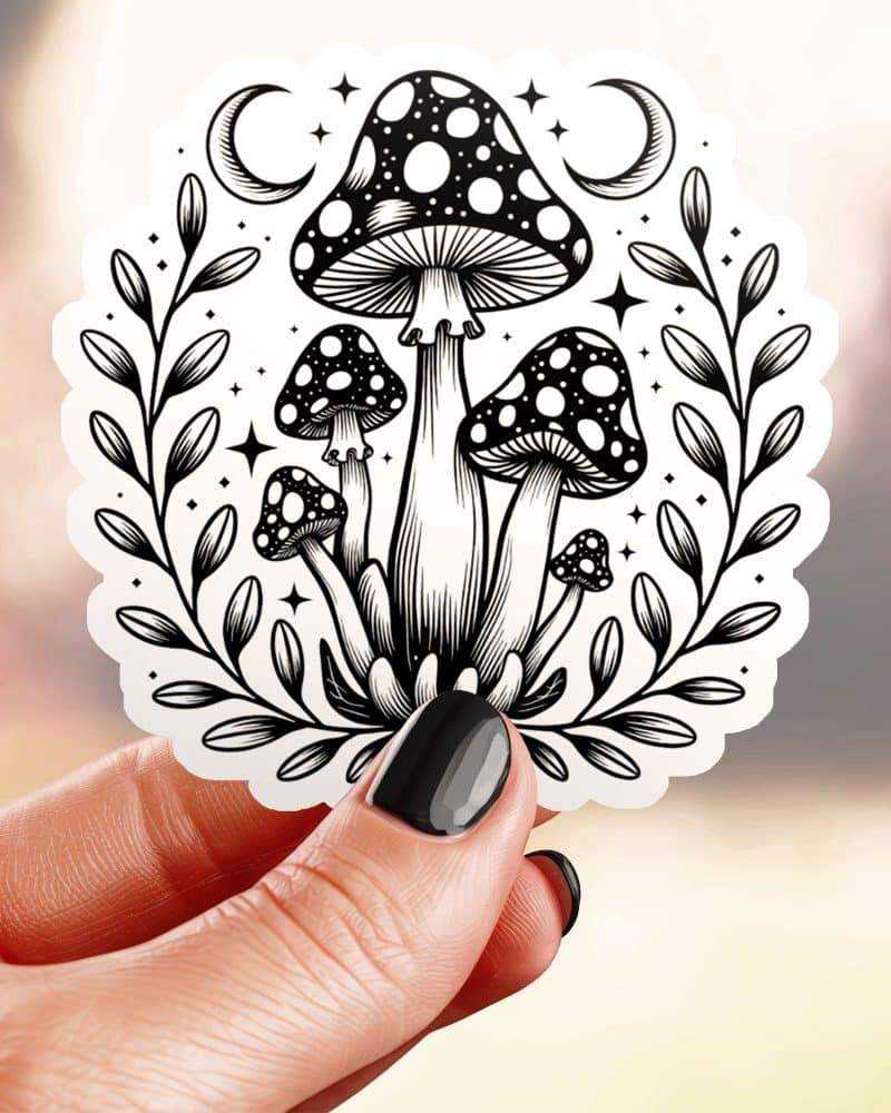 Black and white sticker of several mushrooms with crescent moons and stars in a leafy wreath.