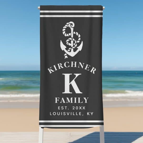 Black Beach Towel With A White Anchor, The Name Kirchner, A Large K, And Family Establishment Details.