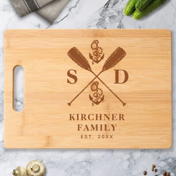 Light Brown Bamboo Cutting Board With A Dark Brown Engraved Design: Crossed Oars, Anchor, And The Kirchner Family Name And Established Year.