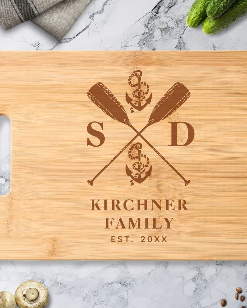 Light brown bamboo cutting board with a dark brown engraved design: crossed oars, anchor, and the Kirchner family name and established year.