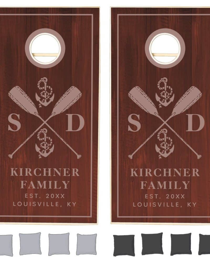 Pair of dark brown wooden cornhole boards, each featuring a nautical design with crossed oars, an anchor, and family initials.