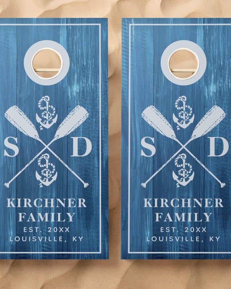 Two blue cornhole boards with a nautical design. Each board features crossed oars, an anchor, and family initials. The Kirchner family name and location are also included.