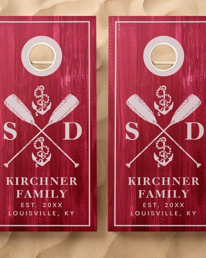 Pair of maroon cornhole boards with a nautical theme, featuring crossed oars, an anchor, and family initials.