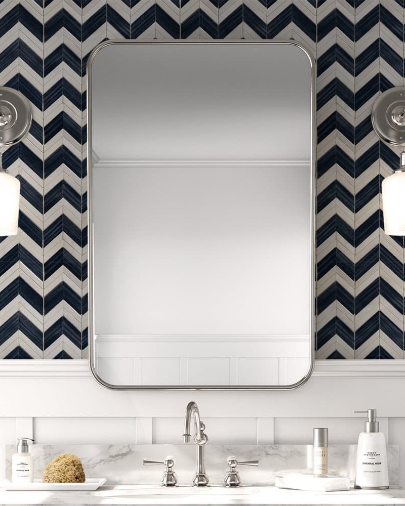 Bathroom vanity with a rectangular mirror flanked by wall-mounted lights, all set against a herringbone patterned tile backsplash.