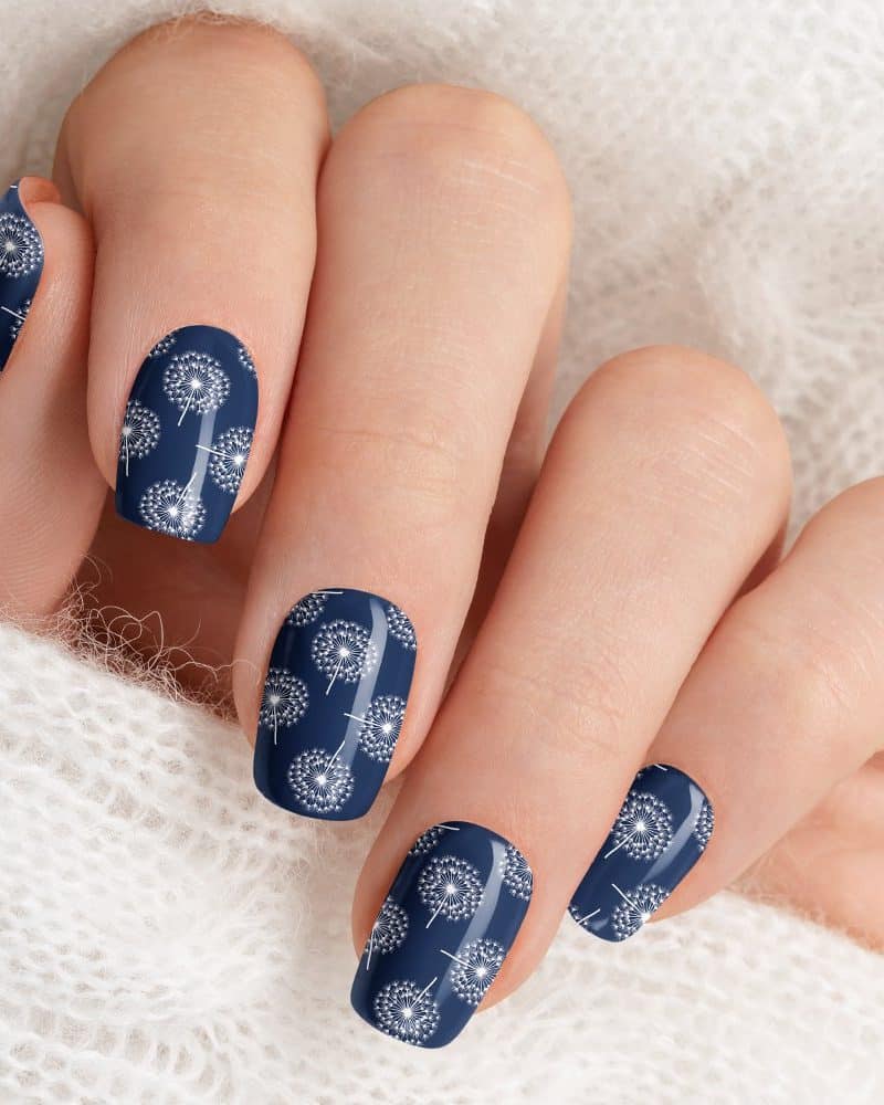 Close-up of a hand with dark blue nails decorated with a white dandelion pattern.