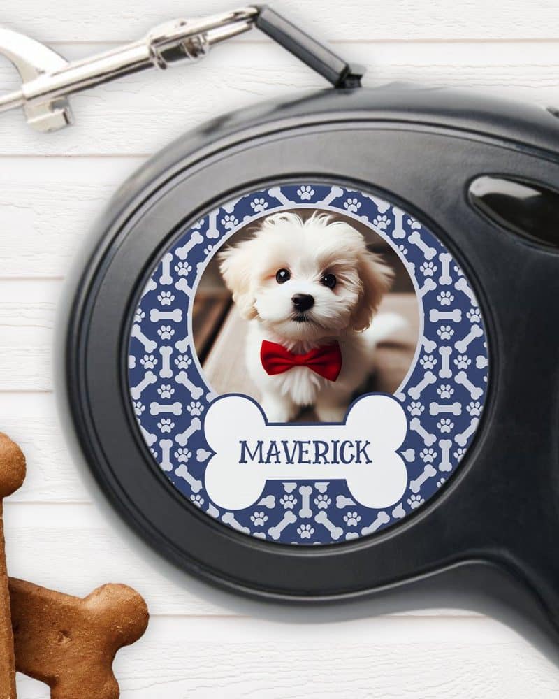 A retractable dog leash with a personalized design featuring a photo of a small white dog wearing a red bow tie. The dogs name, Maverick, is printed on the leash.