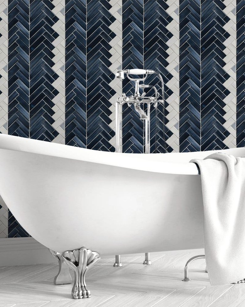 White clawfoot bathtub in front of a dark blue and white herringbone tile wall.